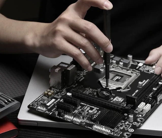 A person working on a desktop motherboard with a screwdriver