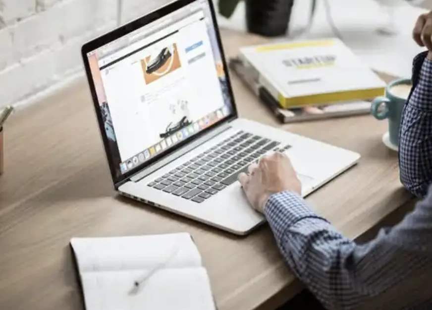 A person browsing a website on a laptop beside a notebook