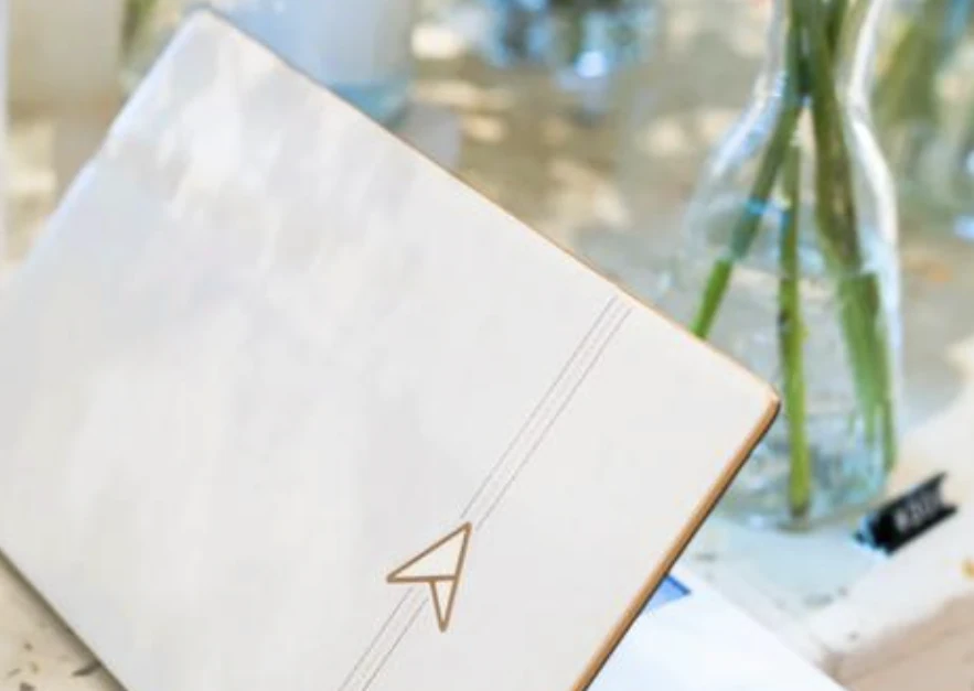 A closed white laptop on a table beside a glass vase