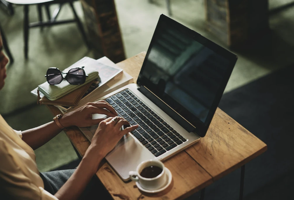 A person using a laptop at a cafe table beside a cup of coffee